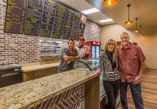 The Paisan's family at the deli counter, in front of the menu wall