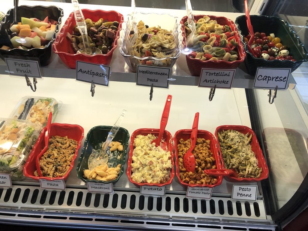 The deli case of house salads, labeled bowl by bowl